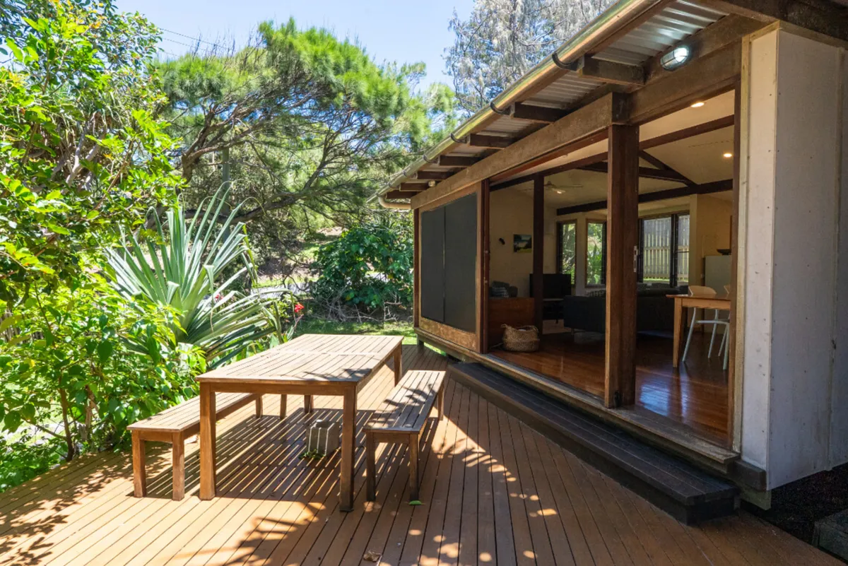 Wooden patio furniture on a sunlit deck beside sliding doors